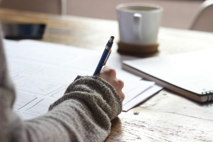 Photo by Unseen Studio person writing on brown wooden table near white ceramic mug